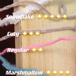 May include: Four different types of yarn are shown on a wooden surface. The yarn types are labeled "Snowflake", "Cuty", "Regular", and "Marshmallow". Each yarn type is rated with a star rating system, with five stars being the most difficult and one star being the easiest. Snowflake is rated five stars, Cuty is rated three stars, Regular is rated two stars, and Marshmallow is rated four stars.