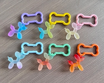 Könnte beinhalten: Eine Sammlung bunter Schlüsselanhänger mit einem Ballonhund-Design. Die Schlüsselanhänger sind in verschiedenen Farben erhältlich, darunter Lila, Gelb, Rosa, Blau, Grün und Orange. Jeder Schlüsselanhänger hat einen Verschluss zur einfachen Befestigung.