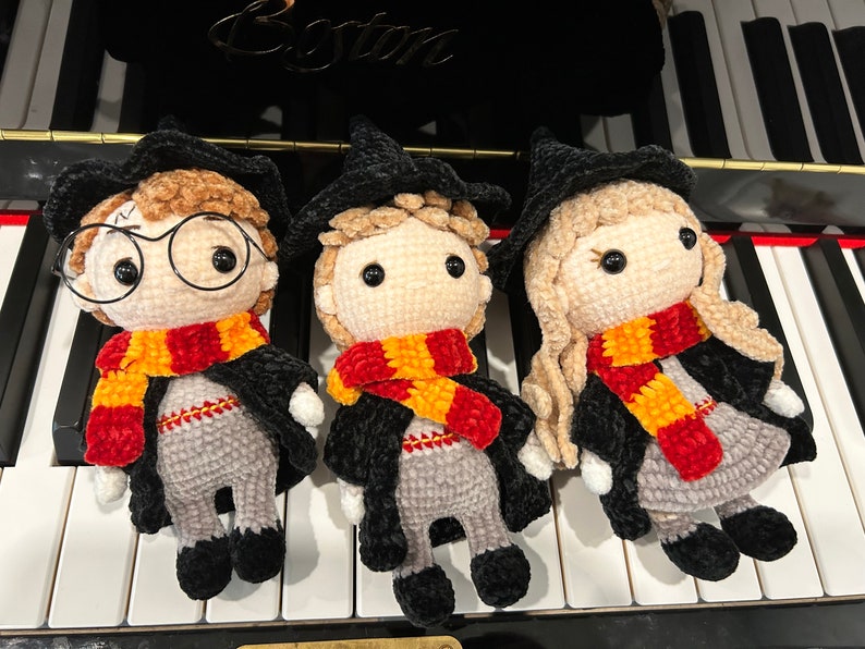 May include: Three crocheted Harry Potter characters, each wearing a black robe and a red and yellow scarf. The characters are standing on a white and black keyboard.