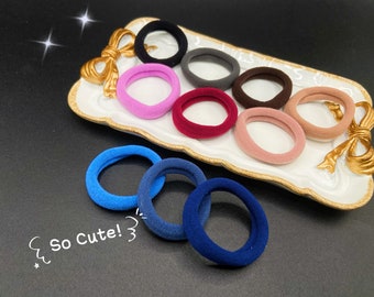 May include: A set of colorful hair ties in a variety of colors, including pink, red, brown, gray, and black. The hair ties are arranged on a white plate with a gold bow. The text "So Cute!" is written on the image.