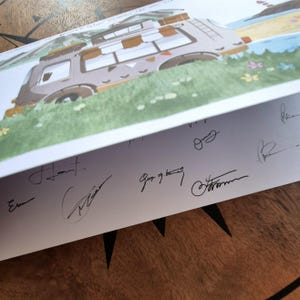 May include: An illustration of a camper van parked on a grassy area near a beach. The artwork features a brown and tan van with several windows and a roof rack. The bottom edge of the artwork displays several signatures.