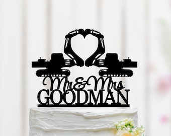 May include: Black silhouette of two construction vehicles forming a heart shape with the text "Mr. & Mrs. GOODMAN" below. The topper is on a white wedding cake.