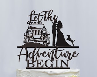 Peut inclure: Un cake topper noir avec le texte "Let The Adventure Begin". Le topper représente une silhouette d'une jeep, d'un couple et d'un chien. Le gâteau est blanc avec des décorations florales.