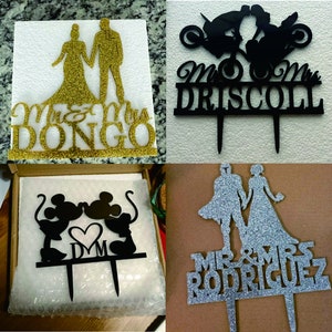 May include: Four different cake toppers featuring a bride and groom. The first topper is gold glitter with the text "Mr. & Mrs. Dongo". The second topper is black with the text "Mr. & Mrs. Driscoll" and a motorcycle design. The third topper is black with a Mickey Mouse and Minnie Mouse design and the text "D&M". The fourth topper is silver glitter with the text "Mr. & Mrs. Rodriguez".