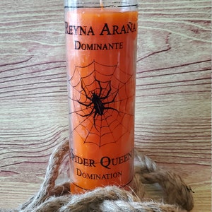 Puede incluir: Vela naranja con un diseño de telaraña y araña negra. El texto de la vela dice "REYNA ARAÑA DOMINANTE SPIDER QUEEN DOMINATION". La vela está en un tarro de cristal transparente, con una mecha blanca. Una cuerda está en primer plano.