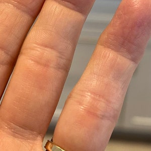 May include: A gold band ring with a thin, polished band.