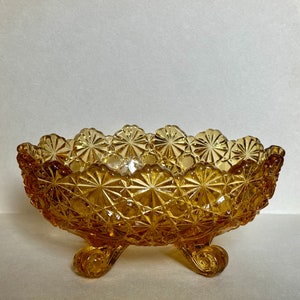 May include: A vintage amber glass bowl with a scalloped edge and a diamond pattern. The bowl has three short legs and is perfect for serving snacks or desserts.