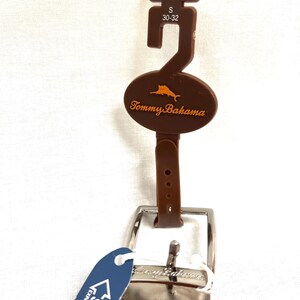 Puede incluir: Cintur&oacute;n reversible marr&oacute;n con hebilla plateada. El cintur&oacute;n tiene una etiqueta marr&oacute;n con el logo de Tommy Bahama y una etiqueta de talla que dice "S 30-32". Una etiqueta azul indica que el cintur&oacute;n se expande hasta 5 cm.
