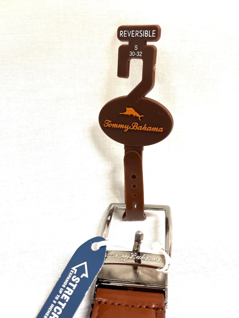 Puede incluir: Cintur&oacute;n reversible marr&oacute;n con hebilla plateada. El cintur&oacute;n tiene una etiqueta marr&oacute;n con el logo de Tommy Bahama y una etiqueta de talla que dice "S 30-32". Una etiqueta azul indica que el cintur&oacute;n se expande hasta 5 cm.