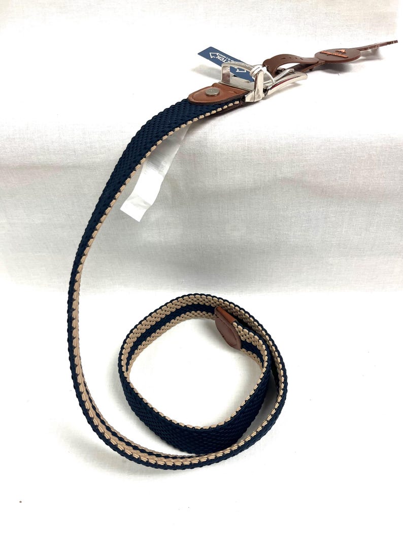 Puede incluir: Un cintur&oacute;n tejido en azul marino y beige con hebilla plateada y detalles en cuero marr&oacute;n. El cintur&oacute;n presenta un dise&ntilde;o a rayas. El cintur&oacute;n es nuevo y tiene una etiqueta adjunta. El cintur&oacute;n mide unos 120 cm de largo.