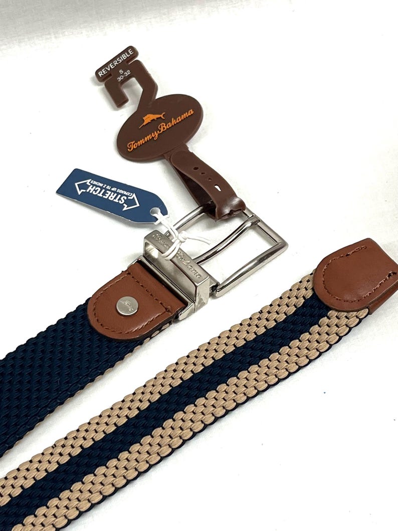Puede incluir: Cintur&oacute;n reversible con dise&ntilde;o tejido en azul marino y beige. El cintur&oacute;n presenta una hebilla plateada y detalles de cuero marr&oacute;n. La etiqueta dice "Tommy Bahama" y "Stretch". Talla del cintur&oacute;n: 76-81 cm.