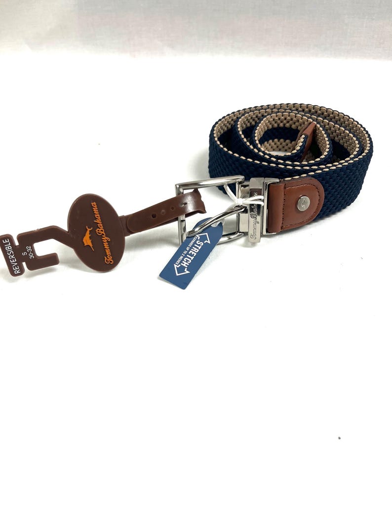 Puede incluir: Cintur&oacute;n reversible con un dise&ntilde;o tejido en azul marino y beige. El cintur&oacute;n tiene una hebilla plateada y detalles en cuero marr&oacute;n. Una etiqueta marr&oacute;n en forma de llave con el logotipo de la marca est&aacute; adjunta, junto con una etiqueta azul "STRETCH".