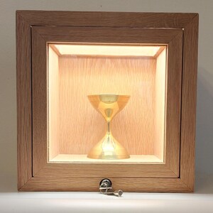 May include: A wooden box with a glass front and a keyhole. Inside the box is a gold-colored chalice.