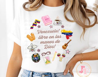 May include: White t-shirt with a vibrant design incorporating Venezuelan symbols. The design includes a map of Venezuela, a Bible, coffee, a guitar, and the text "Venezuela! libre en las manos de Dios!" Floral elements and other Venezuelan icons are also present.