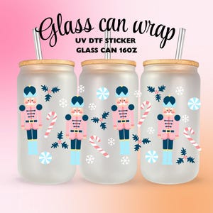 Puede incluir: Tres envoltorios de vidrio esmerilado con tapas de bambú y pajitas de metal. Cada uno presenta un diseño de cascanueces rosa y azul, bastones de caramelo y copos de nieve. El texto "Glass can wrap" y "Glass can 16oz" es visible.