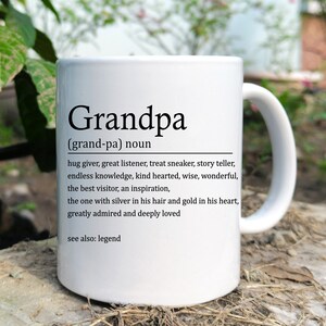 May include: White ceramic coffee mug with a black definition of "Grandpa" printed on it. The definition reads: "(grand-pa) noun hug giver, great listener, treat sneaker, story teller, endless knowledge, kind hearted, wise, wonderful, the best visitor, an inspiration, the one with silver in his hair and gold in his heart, greatly admired and deeply loved see also: legend"