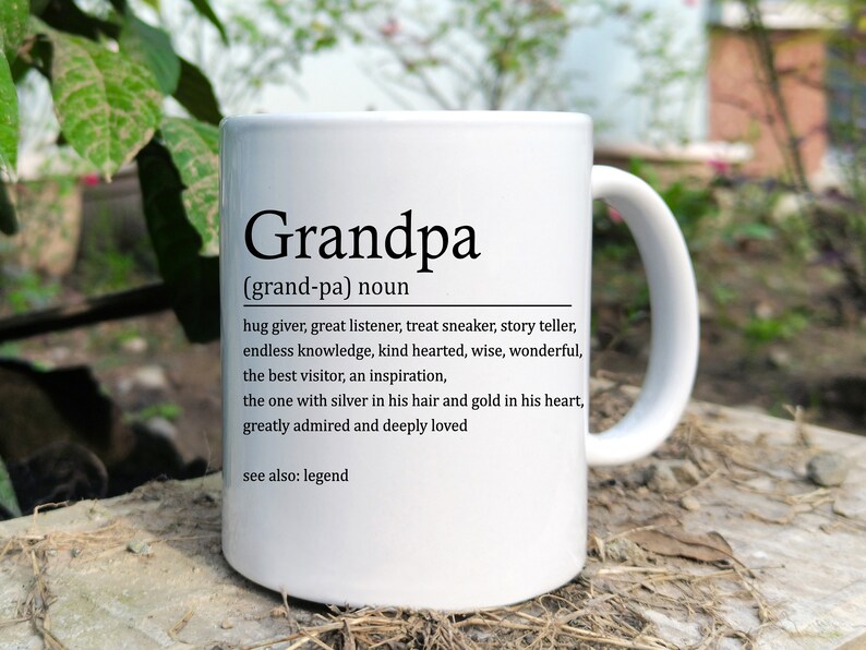 May include: White ceramic coffee mug with a black definition of "Grandpa" printed on it. The definition reads: "(grand-pa) noun hug giver, great listener, treat sneaker, story teller, endless knowledge, kind hearted, wise, wonderful, the best visitor, an inspiration, the one with silver in his hair and gold in his heart, greatly admired and deeply loved see also: legend"