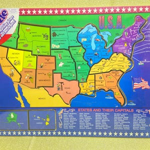 May include: Wooden puzzle of the United States with colorful state outlines and capital names. The puzzle features a matching picture under each piece. The border is blue with white stars and the text "Wooden Puzzle".
