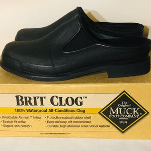 May include: Black waterproof Brit Clogs on a cardboard box. The clogs are made by Muck Boot Company and feature a breathable Airmesh lining and a durable rubber outsole. The box has the text "BRIT CLOG" and "100% Waterproof All-Conditions Clog."