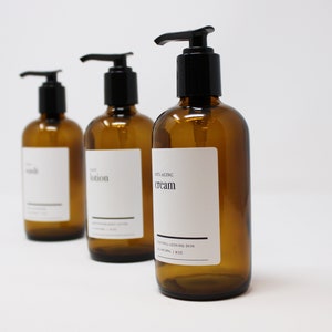 Könnte beinhalten: Drei bernsteinfarbene Glasflaschen mit schwarzen Pumpen und weißen Etiketten. Die Etiketten lauten "wash", "lotion" und "healing cream".