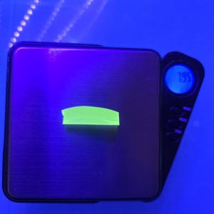 Könnte beinhalten: Ein kleines, neongrünes rechteckiges Objekt liegt auf einer schwarzen Digitalwaage. Die Waage zeigt ein Gewicht von 1,95 an. Der Hintergrund ist hellblau.