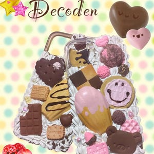 Pode incluir: Uma capa de telefone transparente decorada com v&aacute;rios doces, incluindo biscoitos, chocolate e um cone de sorvete. A capa apresenta um biscoito em forma de cora&ccedil;&atilde;o, uma barra de chocolate e um morango. O texto "Sweets Themed Decoden" est&aacute; no topo.