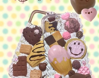May include: A clear phone case decorated with various sweets, including cookies, chocolate, and an ice cream cone. The case features a heart-shaped cookie, a chocolate bar, and a strawberry. The text "Sweets Themed Decoden" is at the top.