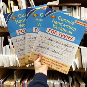 May include: Three identical blue and white cursive handwriting workbooks for teens with a yellow umbrella icon. The cover features the text Cursive Handwriting Workbook FOR TEENS, 100+ PAGES, and Motivational Quotes, Poems & Affirmations.