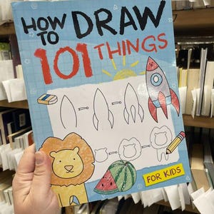 May include: A softcover instructional book titled How to Draw 101 Things for Kids. The light blue cover features a grid pattern, a colorful rocket ship, a yellow lion, and a watermelon illustration, along with step-by-step drawing guides.
