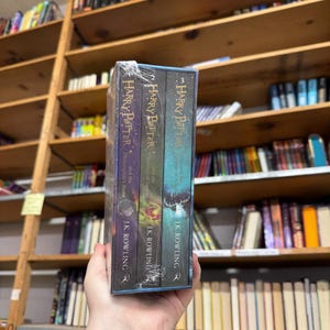 May include: A boxed set of three "Harry Potter" books by J.K. Rowling. The book spines are visible, with titles including "Philosopher's Stone", "Chamber of Secrets", and "Prisoner of Azkaban". The books are in a clear plastic wrap.