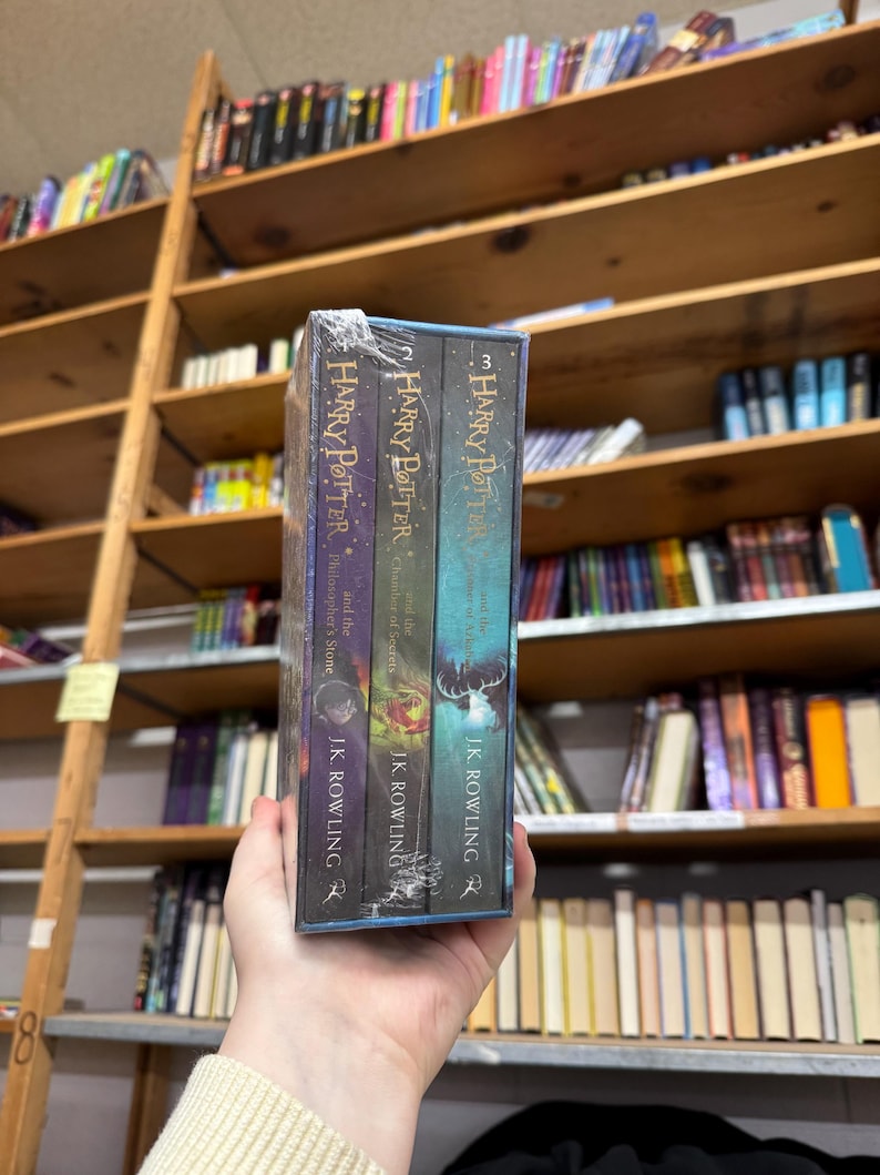 May include: A boxed set of three "Harry Potter" books by J.K. Rowling. The book spines are visible, with titles including "Philosopher's Stone", "Chamber of Secrets", and "Prisoner of Azkaban". The books are in a clear plastic wrap.