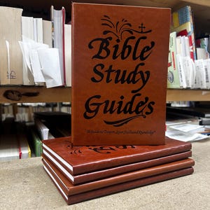 May include: A stack of four brown books with black text on the covers. The top book features the title Bible Study Guide's and the subtitle A Guide to Deepen Your Faith and Knowledge, along with a small cross icon and decorative flourishes.