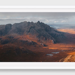 Könnte beinhalten: Eine Panoramaansicht einer zerklüfteten Bergkette mit einem Tal im Vordergrund. Die Berge sind dunkelgrau, und das Tal ist mit einer Mischung aus brauner und grüner Vegetation bedeckt. Der Himmel ist bewölkt, und die Sonne wirft lange Schatten über die Landschaft.