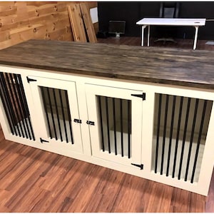 Peut inclure: Cage &agrave; chien en bois blanc avec trois compartiments s&eacute;par&eacute;s, chacun avec une porte en m&eacute;tal noir et un loquet en m&eacute;tal noir. La cage a un dessus en bois brun fonc&eacute;.