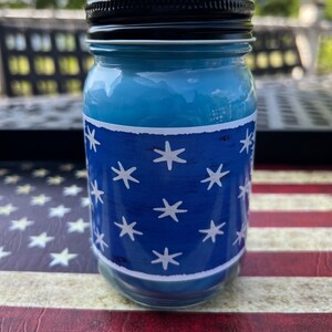 May include: A blue glass jar candle with a white star pattern on a blue background. The jar has a black lid.