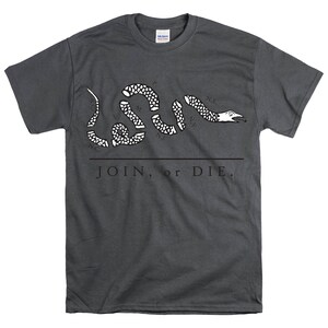 May include: A dark gray t-shirt with a white image of a snake with the words "JOIN, or DIE." printed on the front. The snake is divided into sections, each labeled with the initials of a state:  "N.E.", "N.Y.", "N.J.", "P.", "M.", "V.", "N.C.", "S.C."