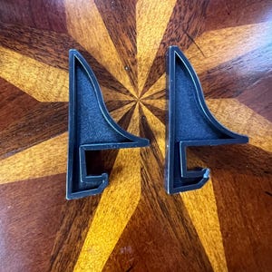 May include: Two black plastic shelf brackets with a triangular shape and a hook on the bottom.