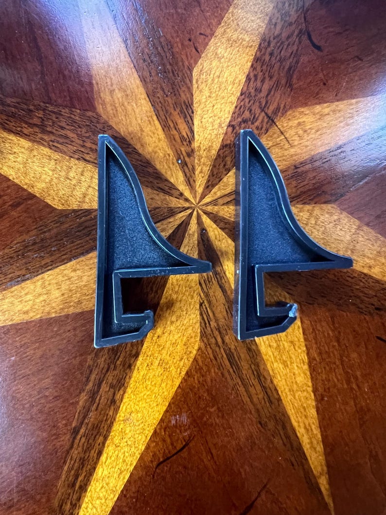 May include: Two black plastic shelf brackets with a triangular shape and a hook on the bottom.