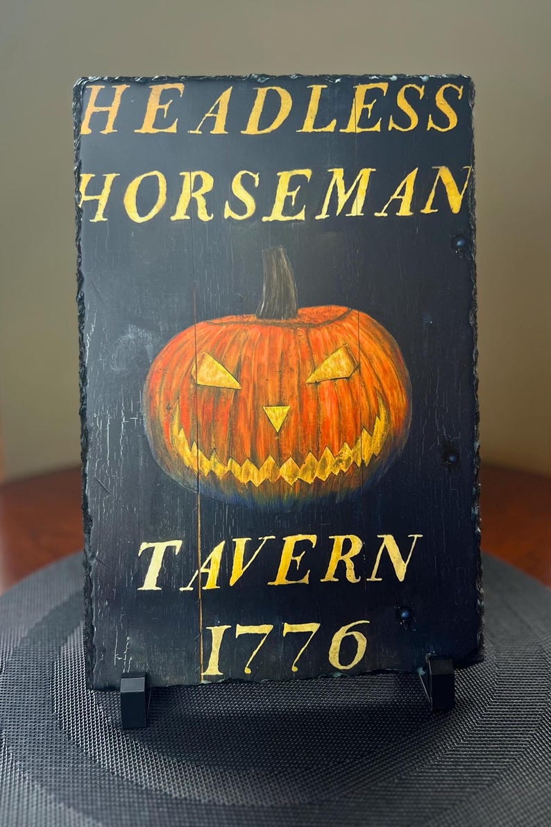 May include: A black slate sign with gold lettering that reads "Headless Horseman Tavern 1776". A carved jack-o'-lantern is in the centre of the sign.