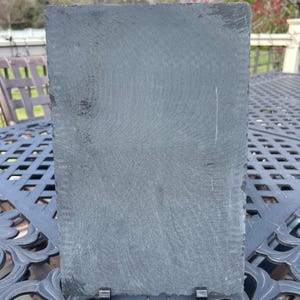 May include: A black slate serving board with a stand. The board has a rough, textured surface.