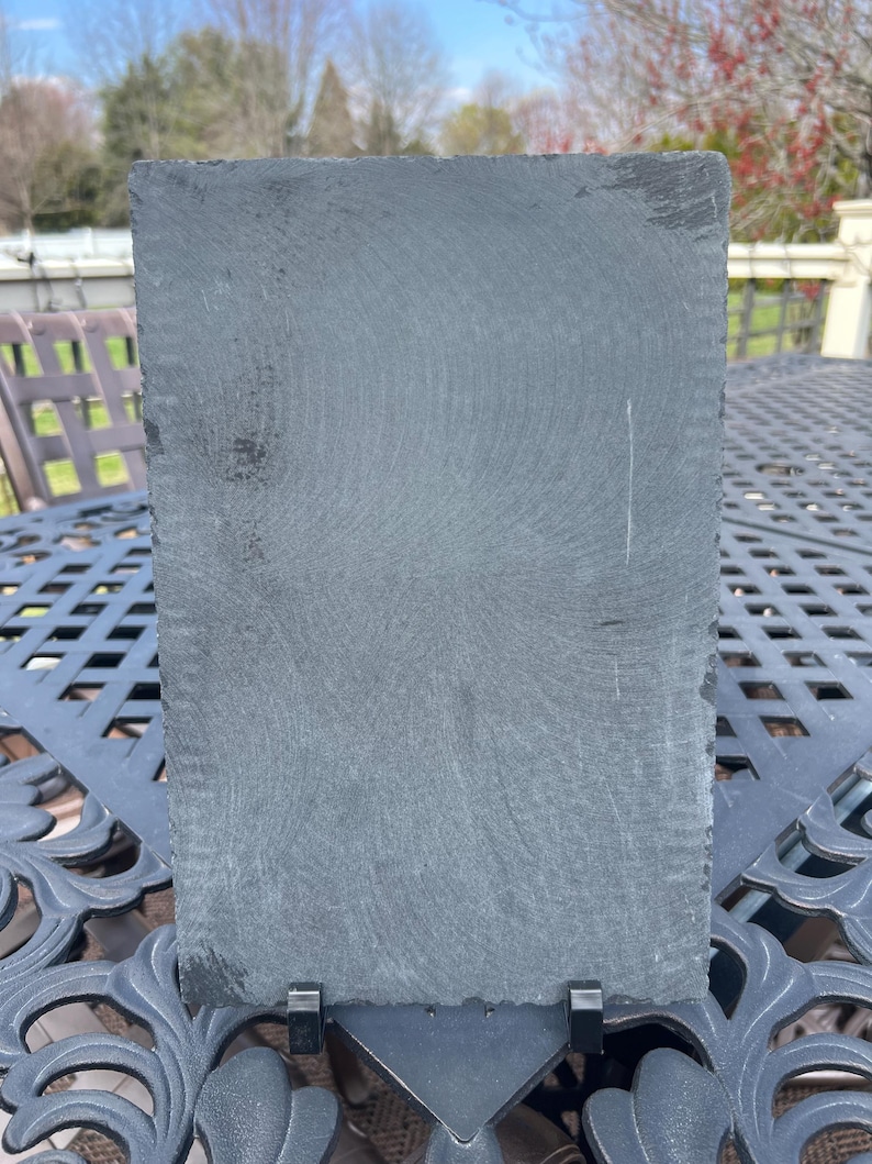 May include: A black slate serving board with a stand. The board has a rough, textured surface.