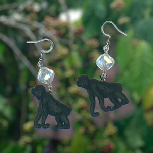 May include: A pair of silver earrings featuring a black monkey charm and a clear crystal bead.
