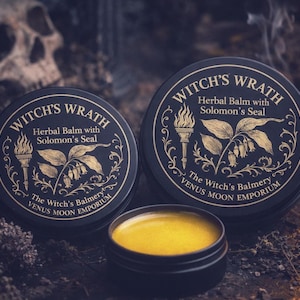 May include: Three black tins of herbal balm with gold detailing. The text on the tins reads "Witch's Wrath" and "Herbal Balm with Solomon's Seal". One tin is open, showing yellow balm. The Witch's Balmery, Venus Moon Emporium.