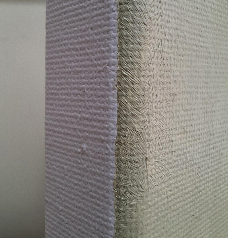 May include: A side view of a rectangular canvas stretched over a wooden frame. The canvas surface features a light beige, textured paint application with visible brushstrokes, while the side edge shows a clean, white, woven fabric texture.