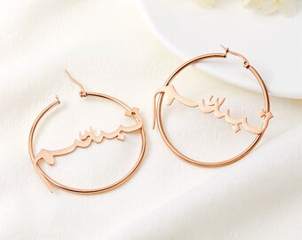 May include: A pair of rose gold hoop earrings with the Arabic word "Yasmin" written in a stylized font.