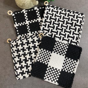 May include: Four black and white woven pot holders with wooden hanging loops. The pot holders feature various geometric patterns, including checks and a houndstooth design. The color scheme is a classic black and white, creating a modern and stylish look for the kitchen.