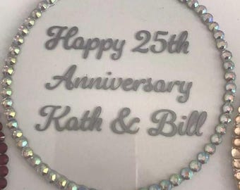 Könnte beinhalten: Ein weißer Tortendekor mit silbernem, schimmerndem Rand und dem Text "Happy 25th Anniversary Kath & Bill".