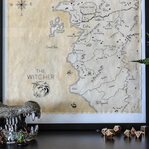 May include: A framed map of the Continent from the Witcher video game series. The map is printed on parchment paper and features a compass, the Great Sea, and various locations including Novigrad, Velen, and Skellige. The map is framed in black and is hanging on a teal wall.