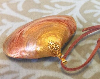 May include: A gold and red painted seashell pendant with a gold filigree charm hanging from a brown leather cord.