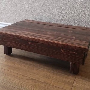 May include: A dark brown wooden step stool with a simple design. The stool has a rectangular top and four legs.